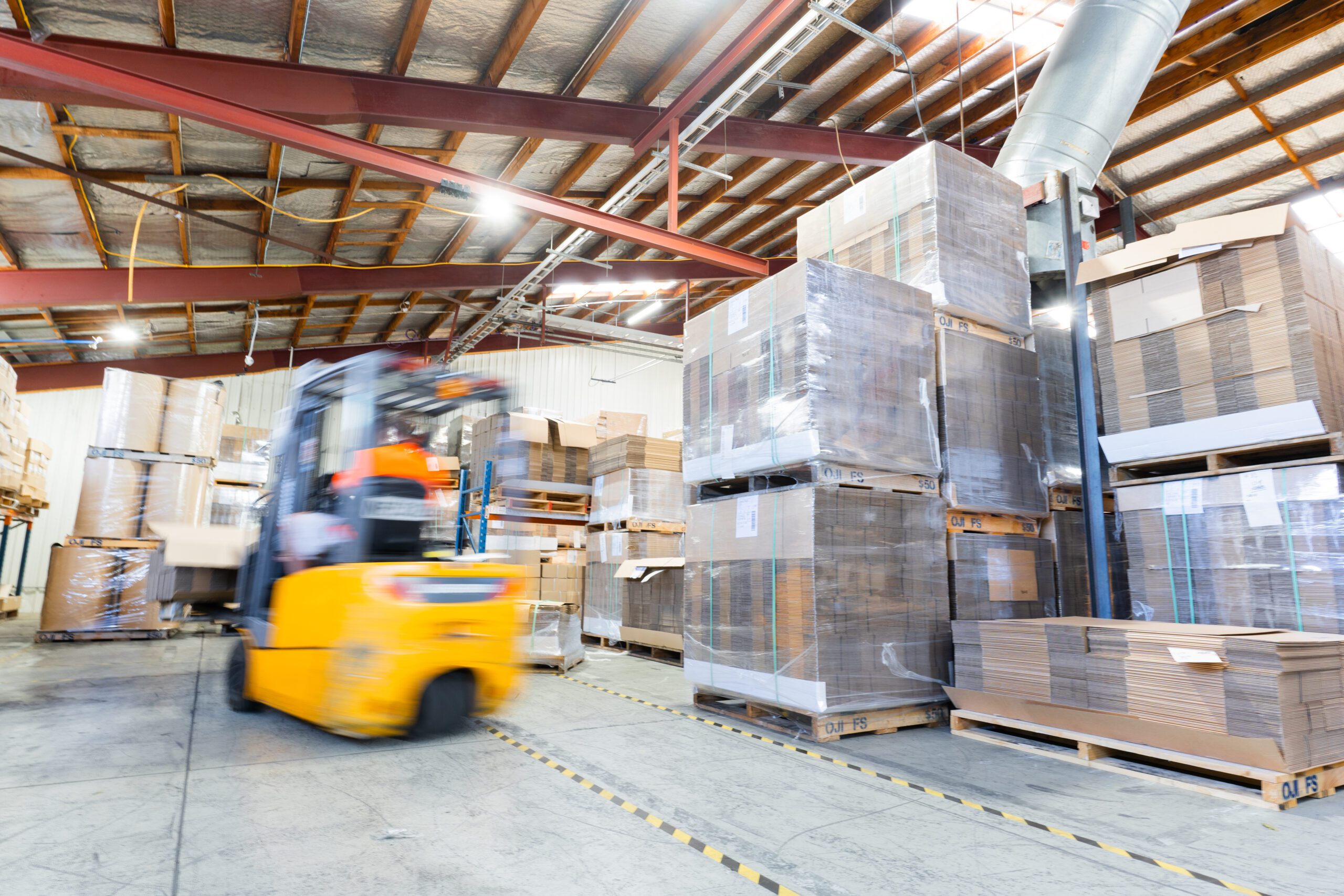 Stacked pallets in warehouse with forklift operating